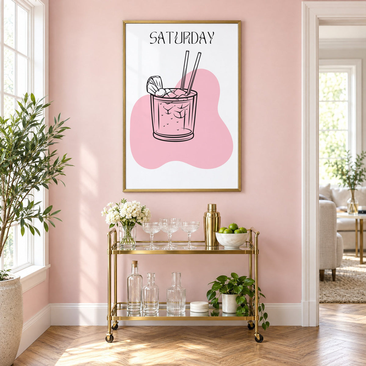 SATURDAY iced cocktail two straws print in a brass frame on a blush pink wall above a gold bar cart with glassware