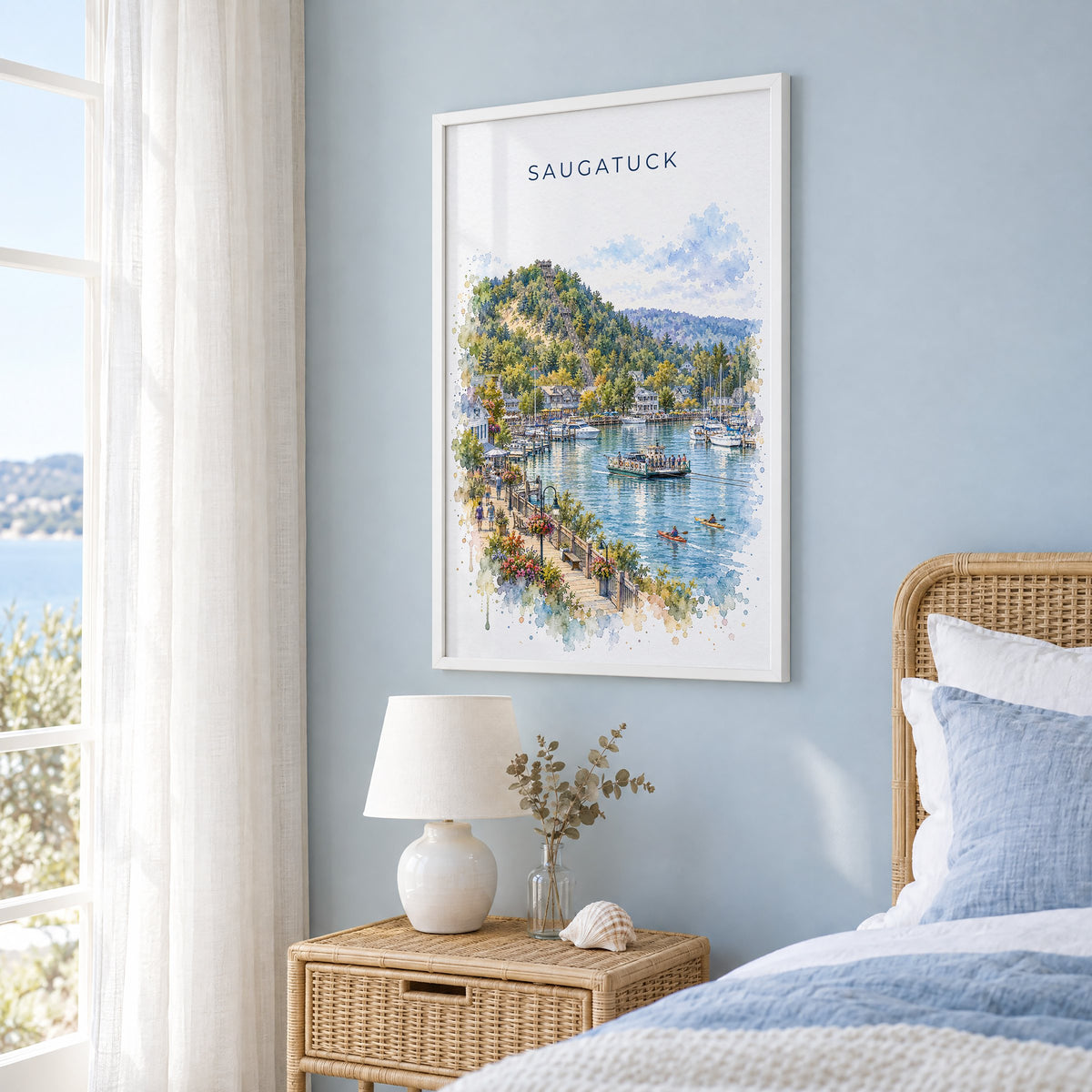 Saugatuck watercolor print in a white frame on a pale blue wall beside a rattan bed in a coastal bedroom