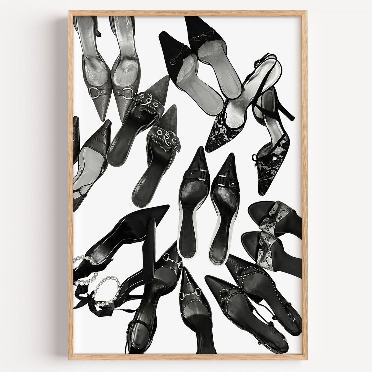 Top-down scattered pointed heels and mules print in a light oak frame on a plain white wall