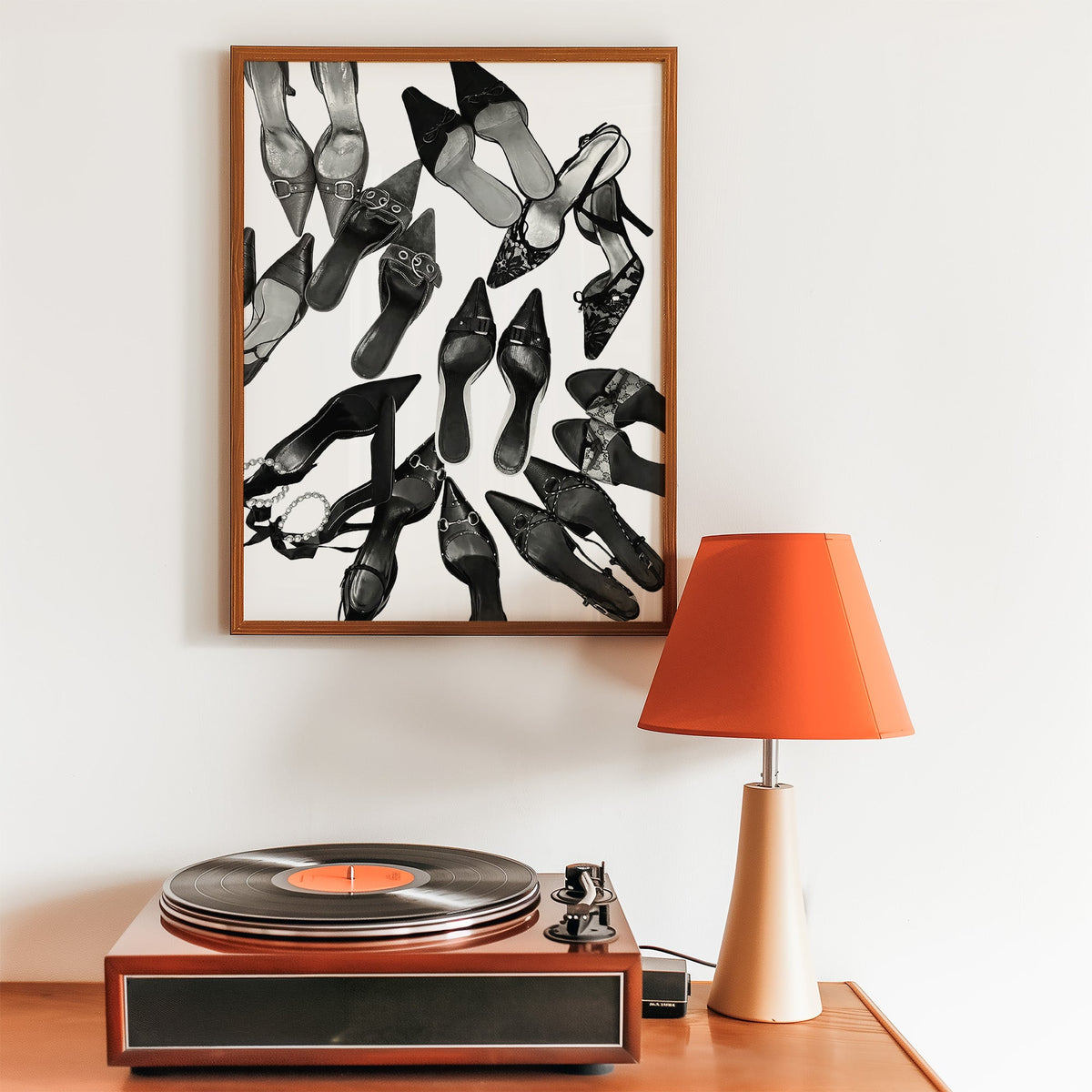 Top-down scattered pointed heels and mules print in a walnut frame above a record player and orange lamp