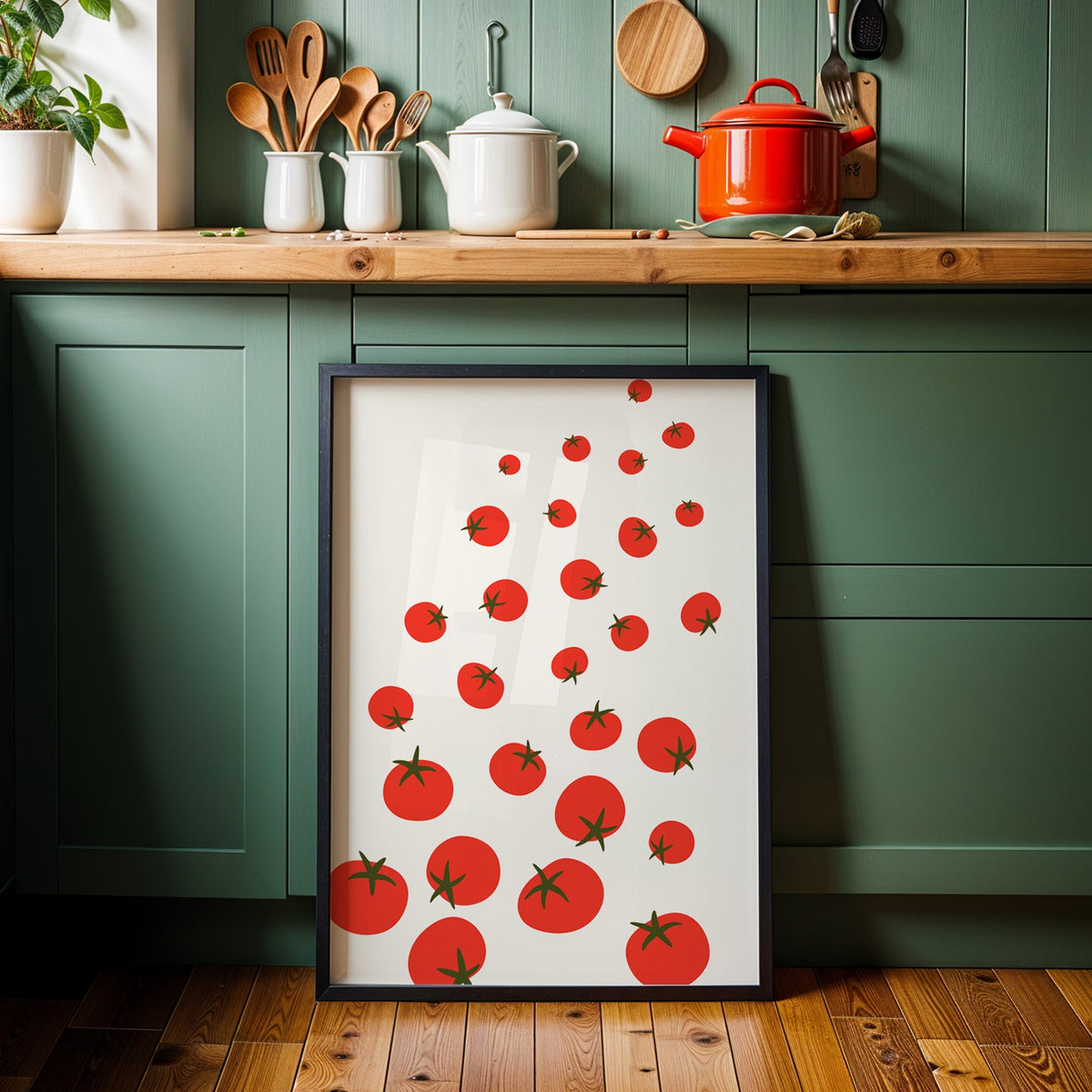 Scattered tomatoes print in a black frame against sage green kitchen cabinets