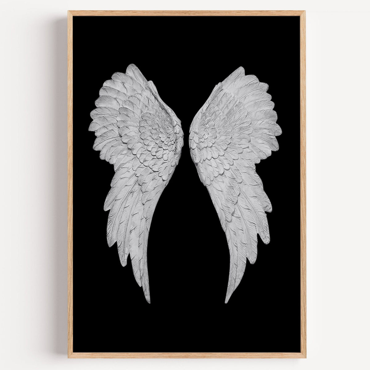 Pair of carved white angel wings on black print in a light oak frame on a plain white wall