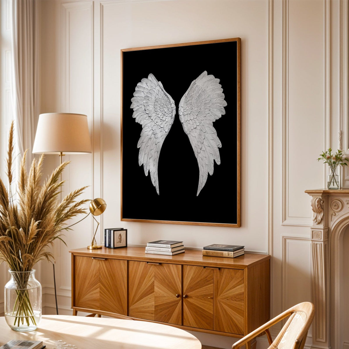 Pair of carved white angel wings on black print in an oak frame above a sunburst wood sideboard with pampas grass