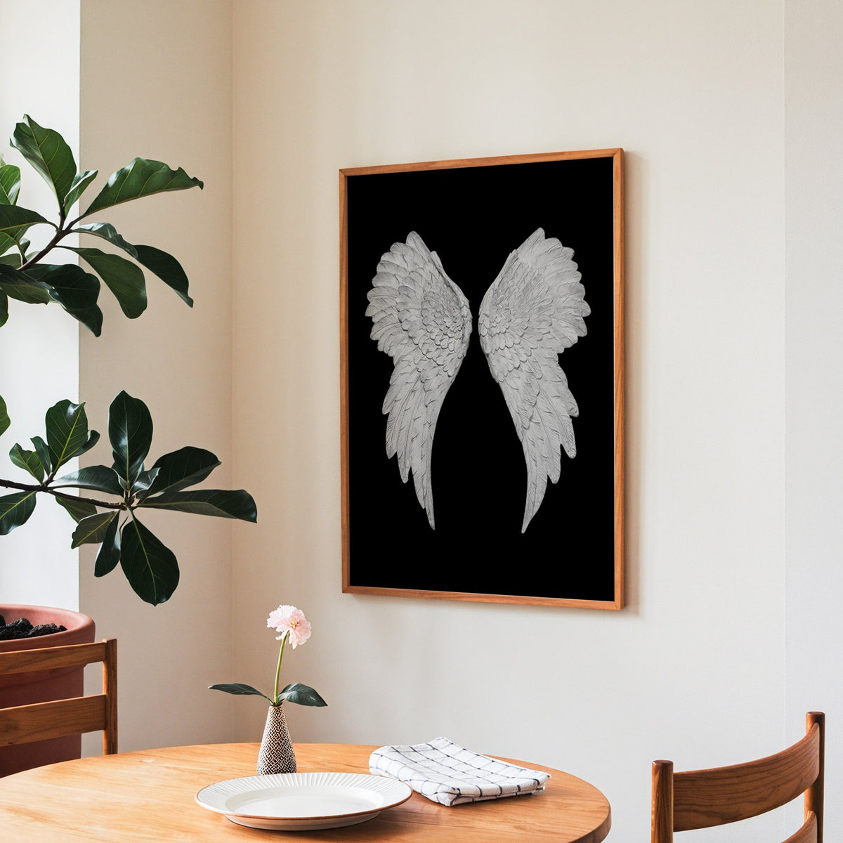 Pair of carved white angel wings on black print in a teak frame above a round wooden dining table