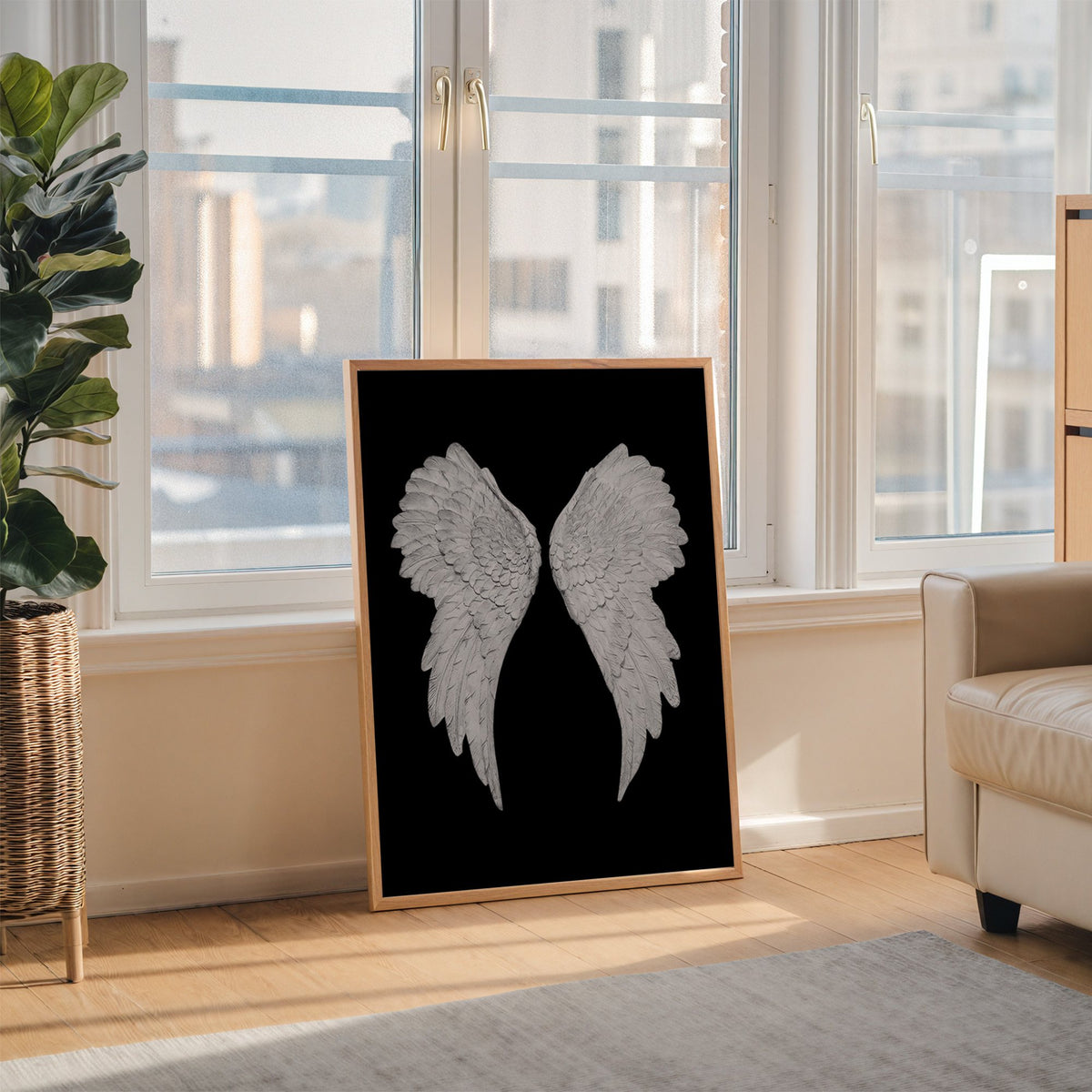 Pair of carved white angel wings on black print in an oak frame leaning on the floor beside a fiddle leaf fig