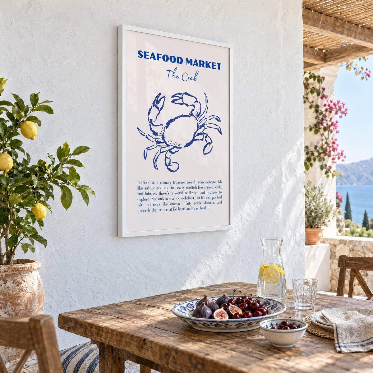 SEAFOOD MARKET The Crab cobalt sketch print in a white frame on a whitewashed terrace wall above a lunch table with figs and cherries, seen at an angle
