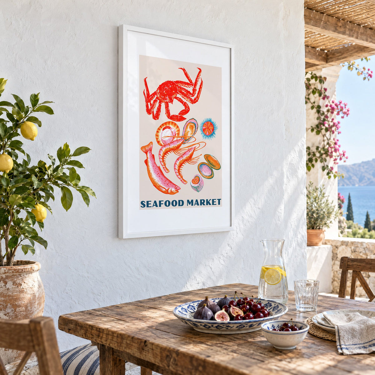 SEAFOOD MARKET gouache crab shellfish print in a white frame on a whitewashed terrace wall above a lunch table with figs and cherries, seen at an angle