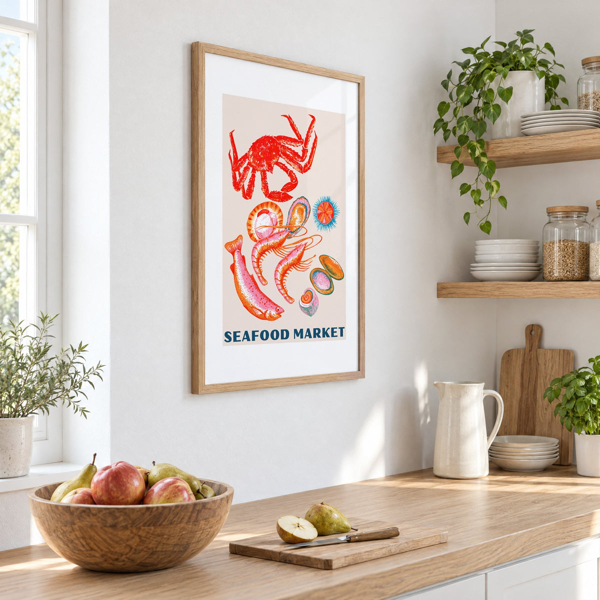 SEAFOOD MARKET gouache crab shellfish print in an oak frame on a white kitchen wall above a counter with apples and pears, seen at an angle