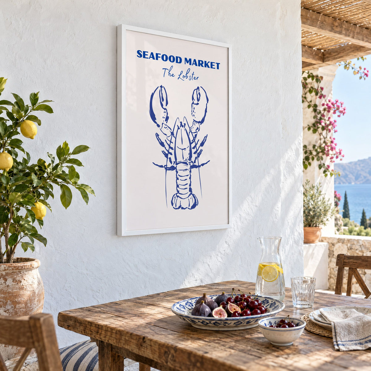 SEAFOOD MARKET The Lobster cobalt sketch print in a white frame on a whitewashed terrace wall above a lunch table with figs and cherries, seen at an angle