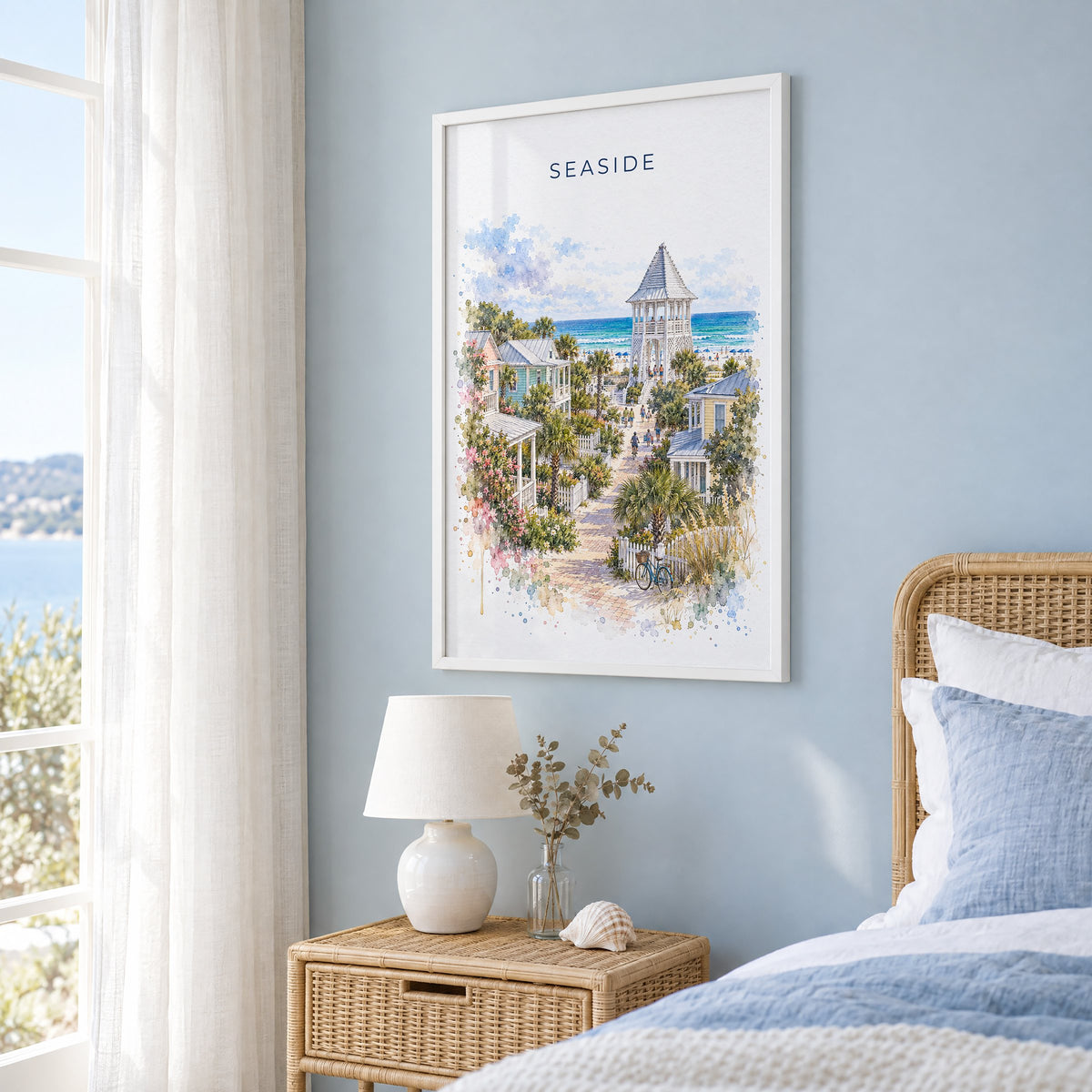 Seaside, Florida watercolor print in a white frame on a pale blue wall beside a rattan bed in a coastal bedroom