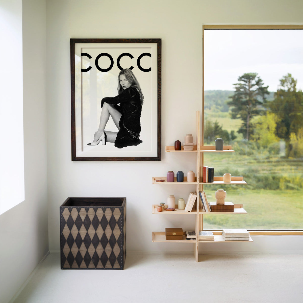 Seated woman in black knit dress under giant letters print in a walnut frame with a white mat beside wooden shelves and a garden window