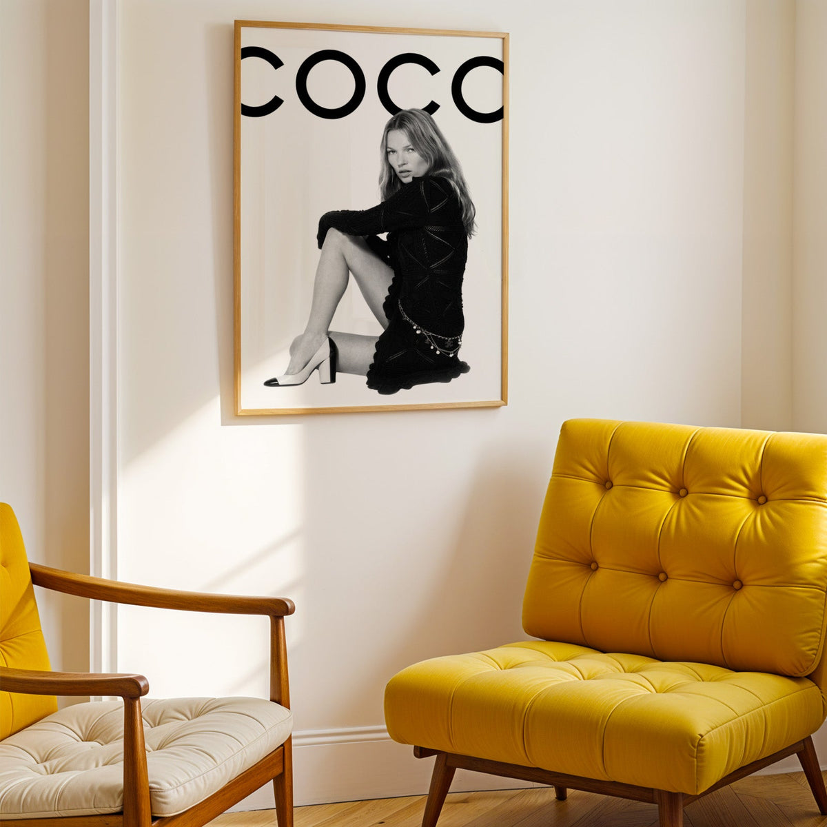 Seated woman in black knit dress under giant letters print shown in a gold frame above a mustard yellow tufted armchair