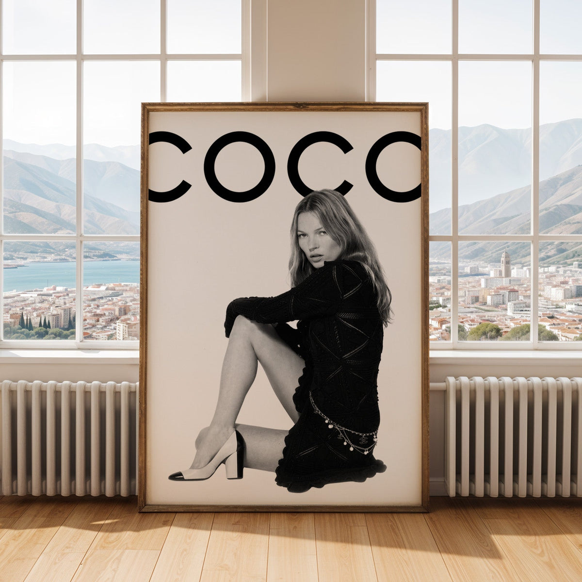 Seated woman in black knit dress under giant letters print shown in an antique gold frame by tall windows with a sea view
