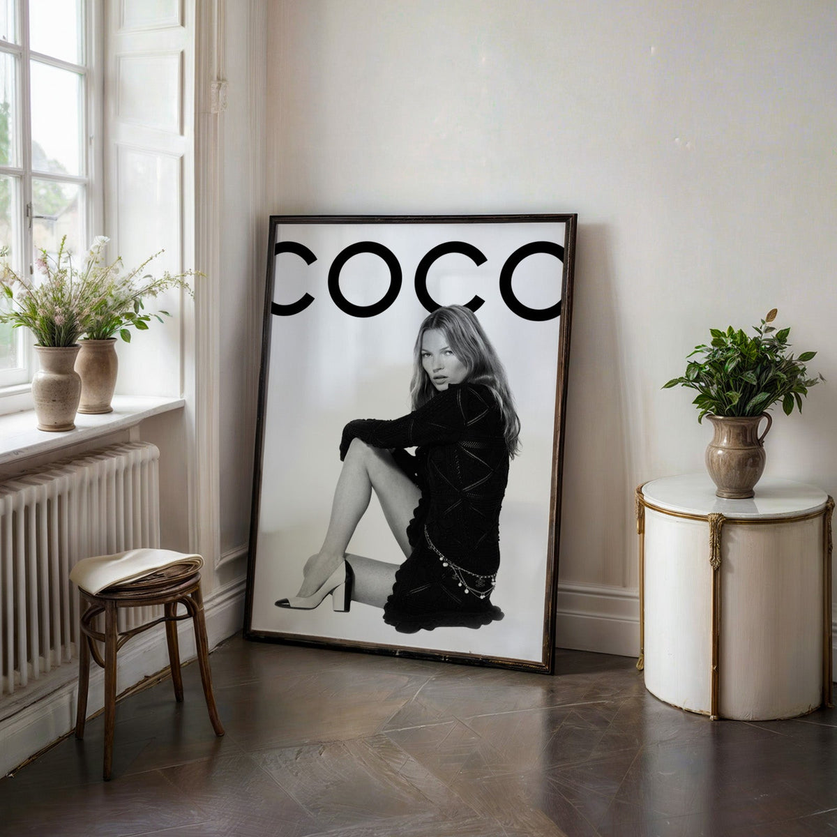 Seated woman in black knit dress under giant letters print in a black frame on a dark stone floor beside a white side table