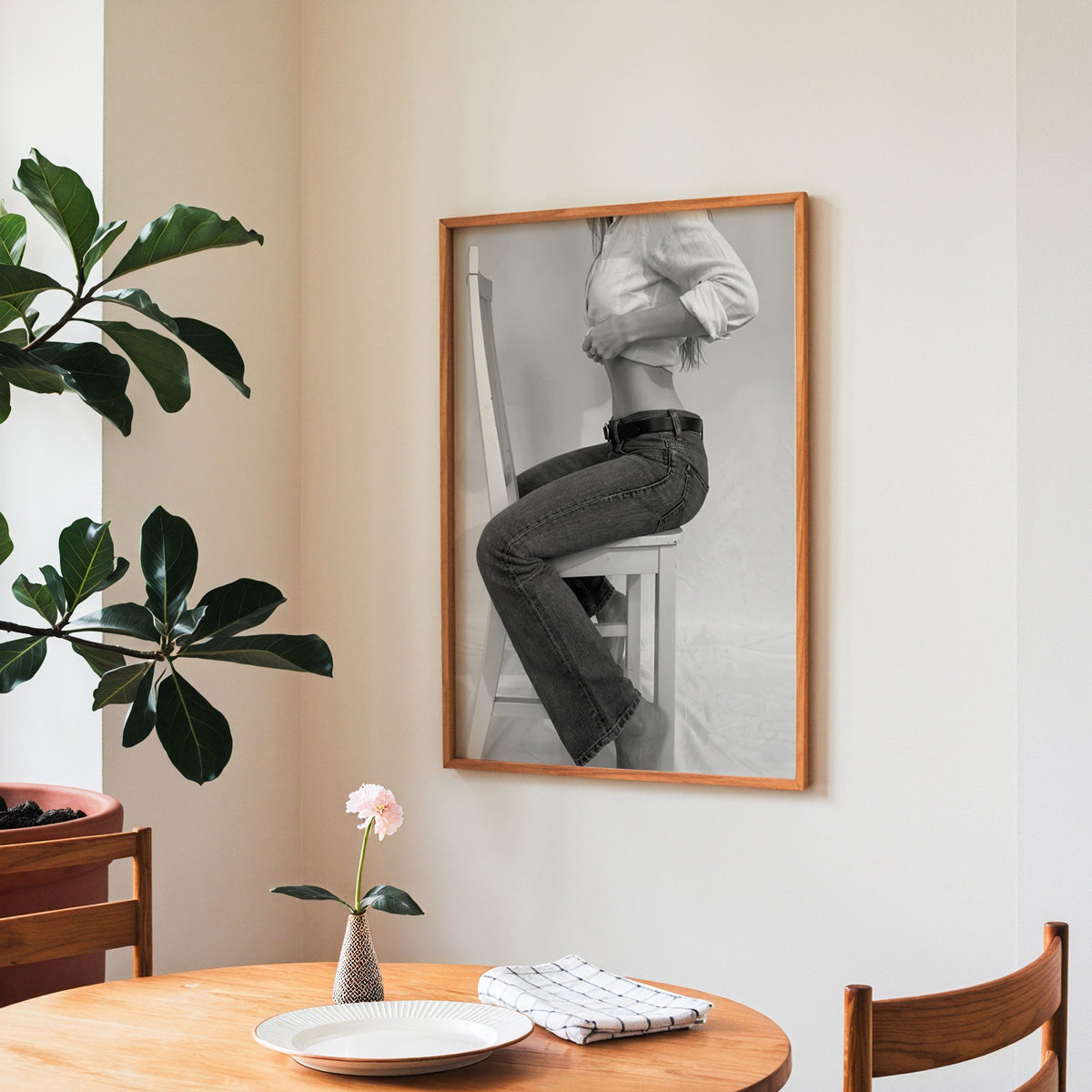 Woman in flared jeans on a white wooden chair print in a teak frame above a round wooden dining table