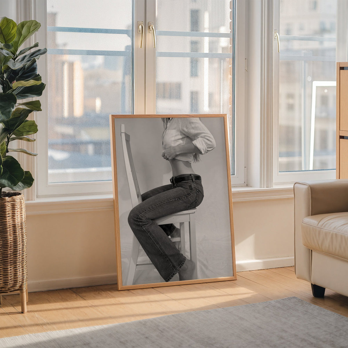 Woman in flared jeans on a white wooden chair print in an oak frame leaning on the floor beside a fiddle leaf fig