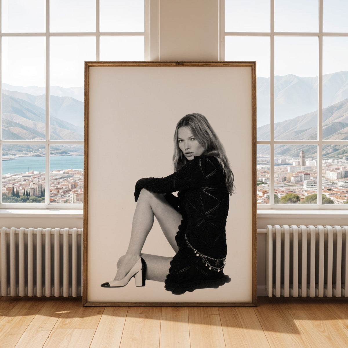Seated woman in lace-pattern knit dress on white print shown in an antique gold frame by tall windows with a sea view
