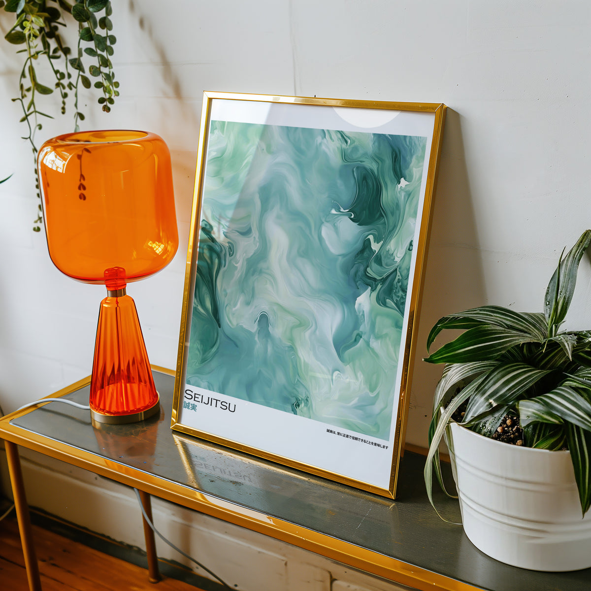 Teal and moss green marble print shown in a gold frame on a console beside an orange glass lamp