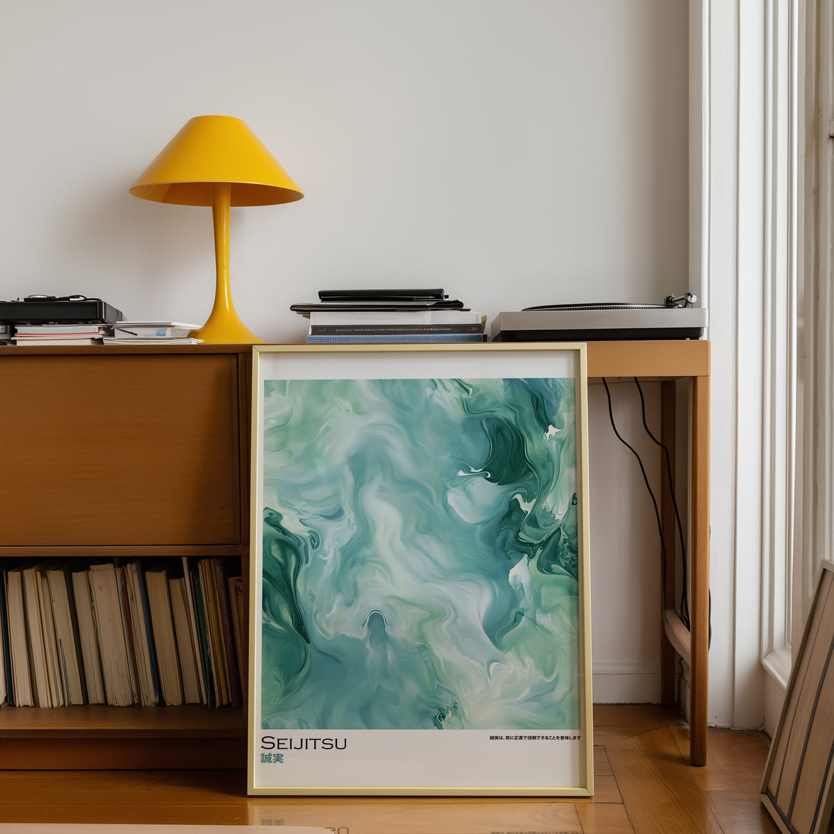Teal and moss green marble print shown in a gold frame below a teak desk with a yellow lamp
