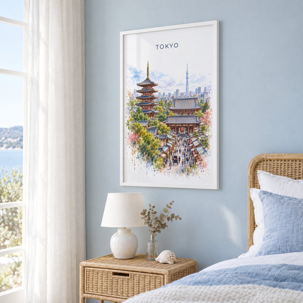 Senso-ji watercolor print in a white frame on a pale blue wall beside a rattan bed in a coastal bedroom