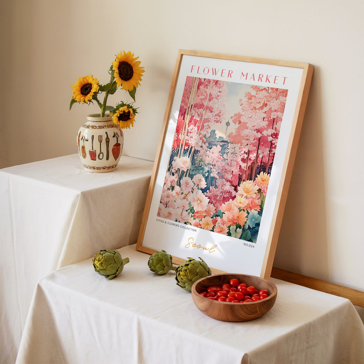 Seoul flower market print in an oak frame leaning on a linen-draped table beside a vase of sunflowers