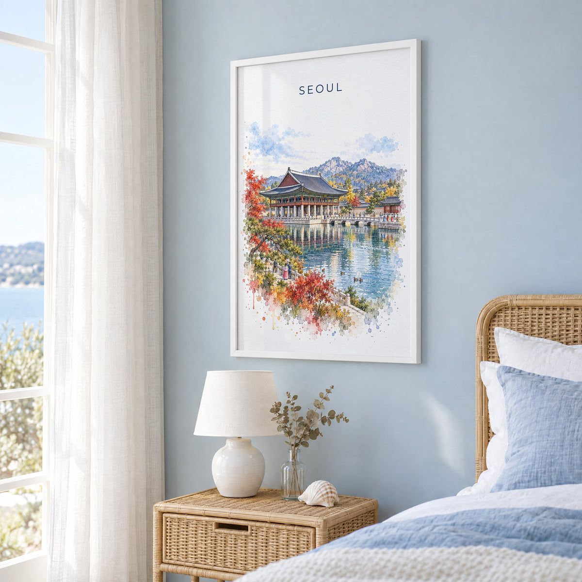 Seoul watercolor print in a white frame on a pale blue wall beside a rattan bed in a coastal bedroom