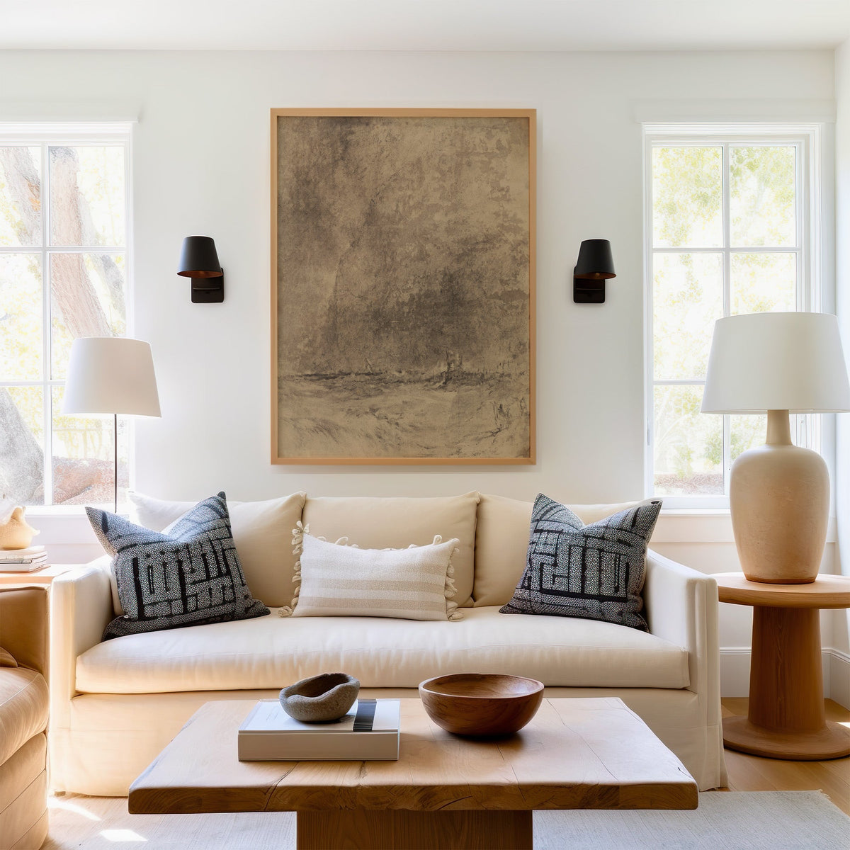 Sepia charcoal storm and tower sketch print in a light oak frame above a cream sofa between two black wall sconces