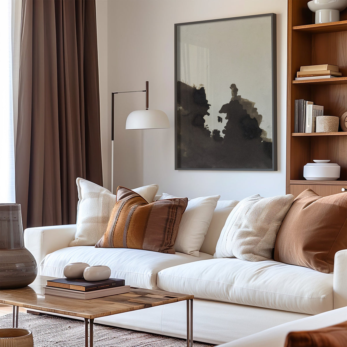 Sepia ink blot facing profiles abstract print in a black frame above a cream sofa with brown striped pillows