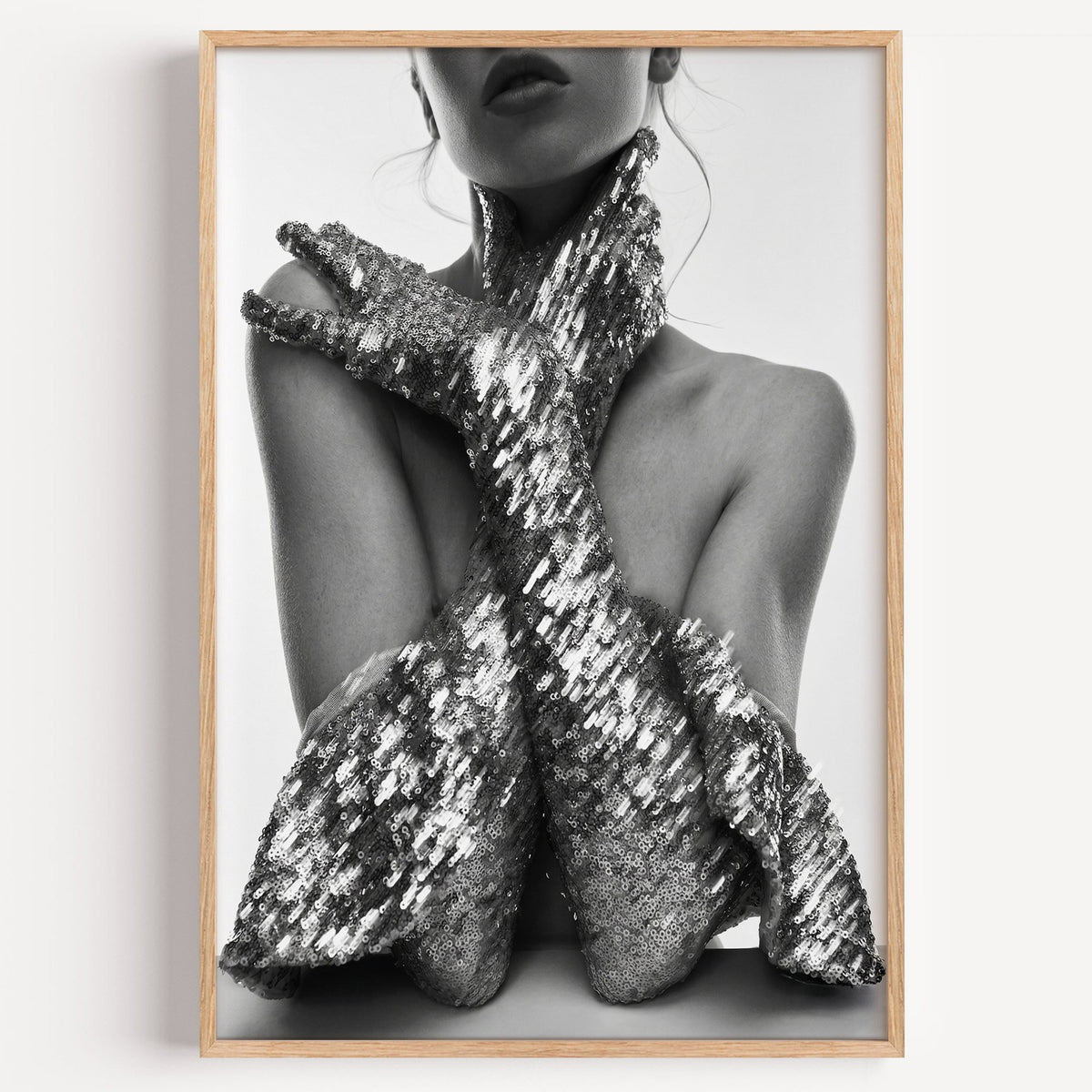 Crossed arms in sequin opera gloves print in a light oak frame on a plain white wall