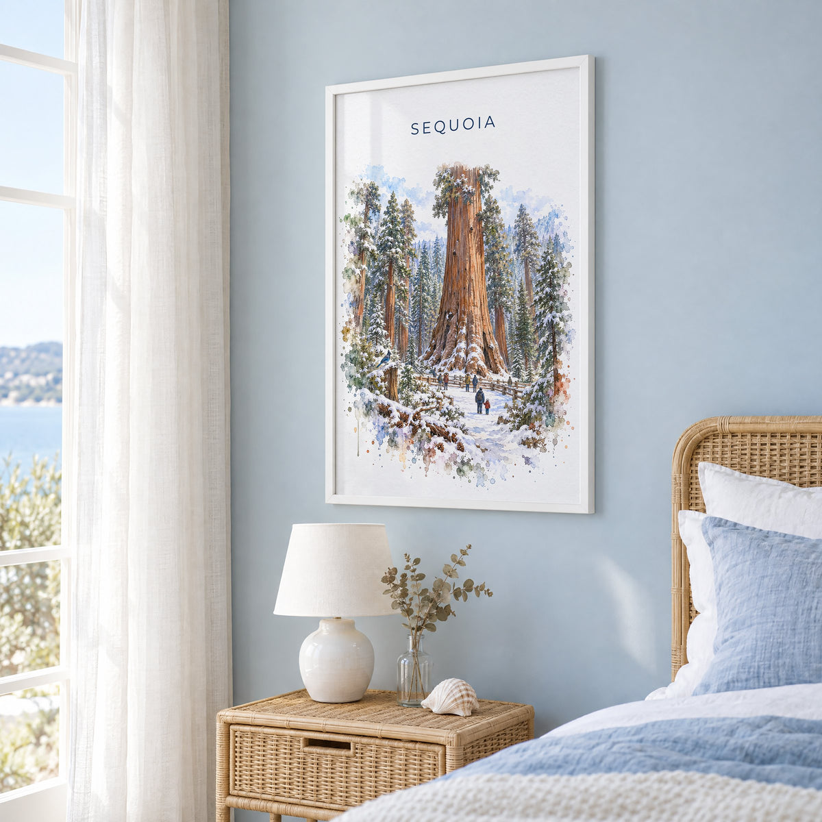 Sequoia National Park watercolor print in a white frame on a pale blue wall beside a rattan bed in a coastal bedroom