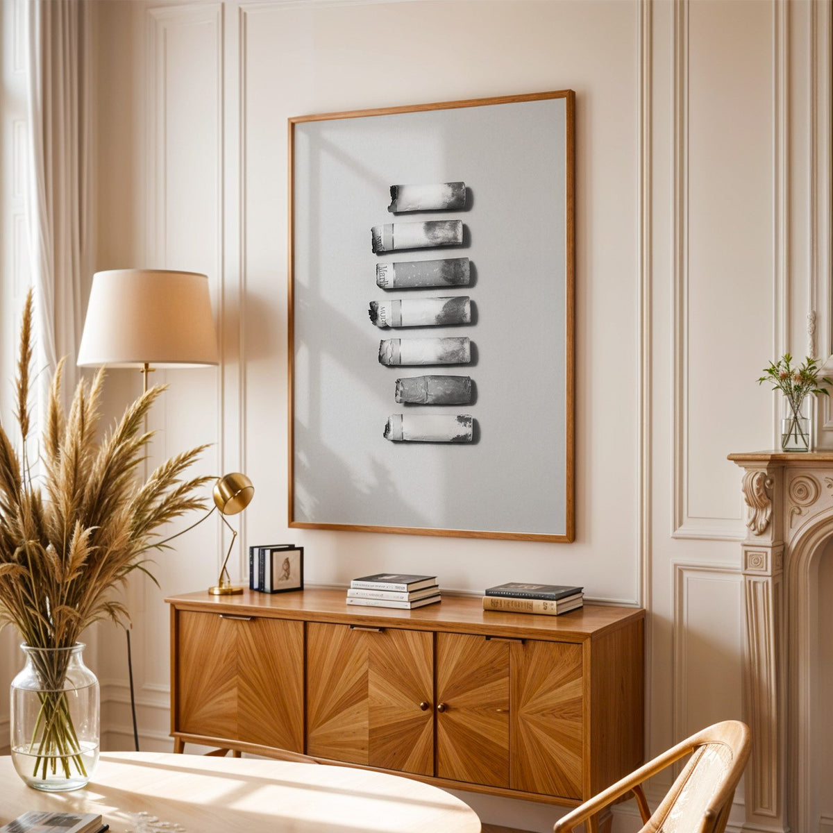 Seven cigarette ends in a column on gray print in an oak frame above a sunburst wood sideboard with pampas grass