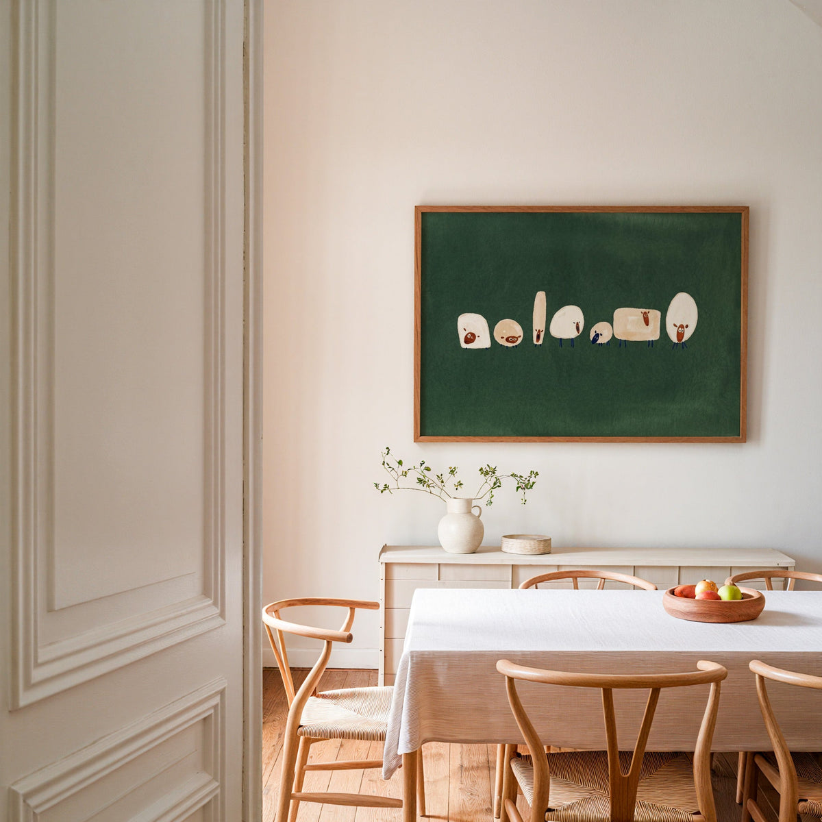 Odd shaped sheep print in an oak frame in a dining room with wishbone chairs