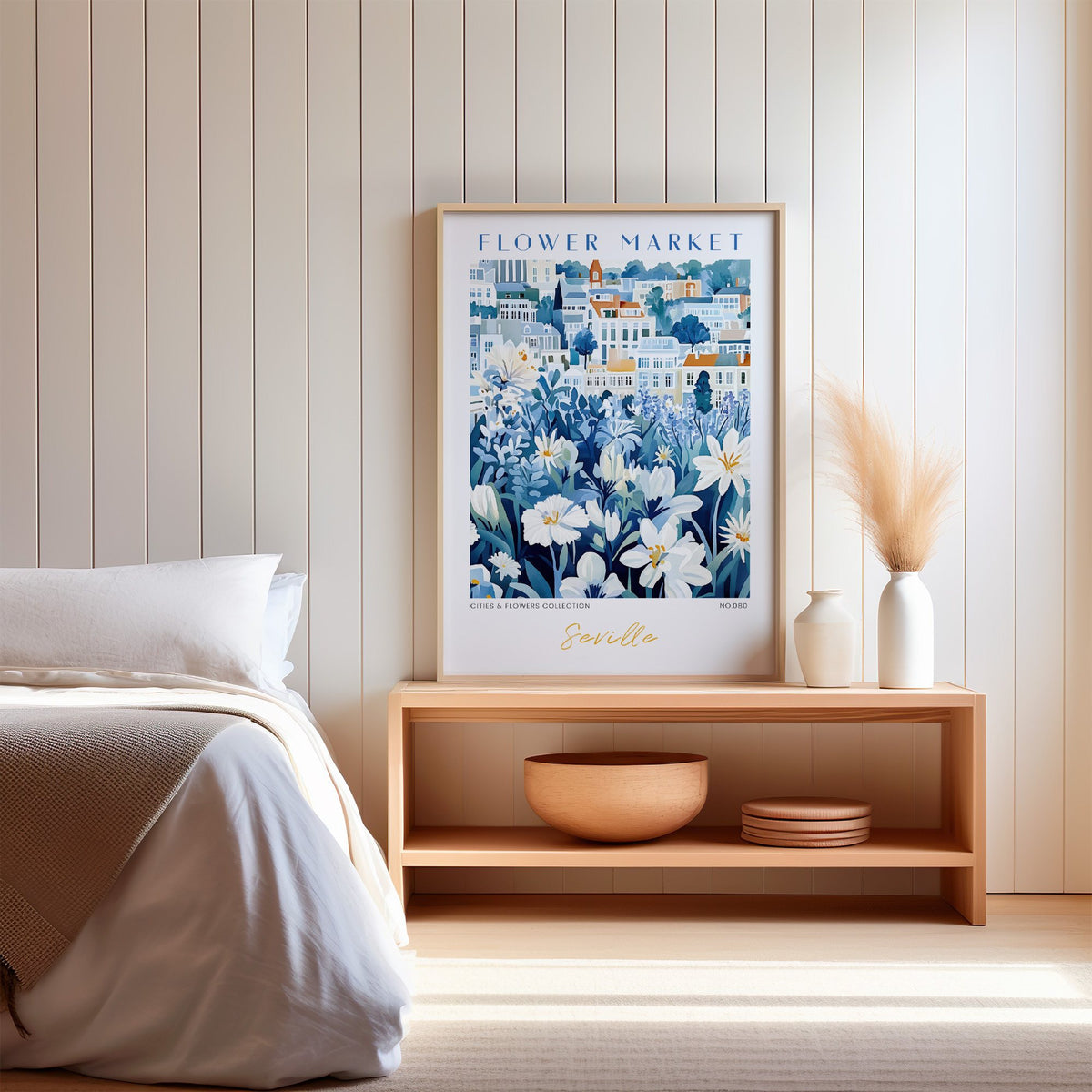 Seville flower market print in an oak frame on a wood bench against a white shiplap bedroom wall with pampas grass