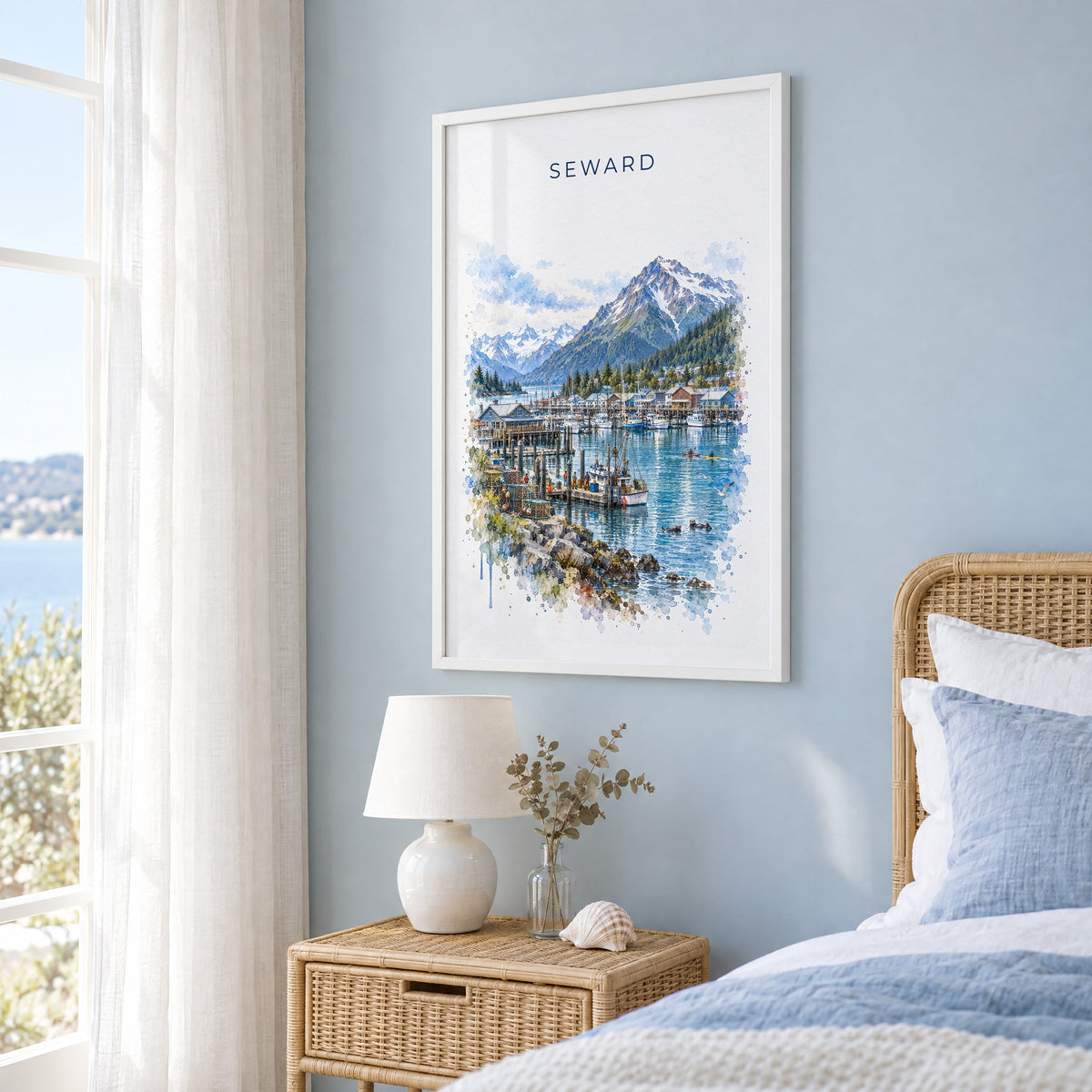 Seward, Alaska watercolor print in a white frame on a pale blue wall beside a rattan bed in a coastal bedroom