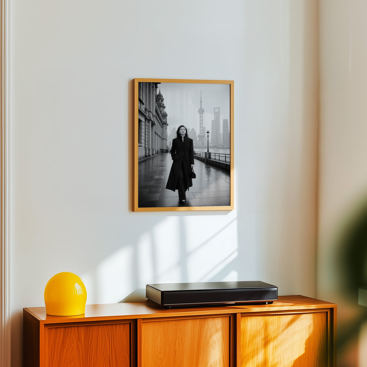 Black and white Shanghai Bund woman in black coat print in an oak frame above a teak sideboard with a yellow glass lamp