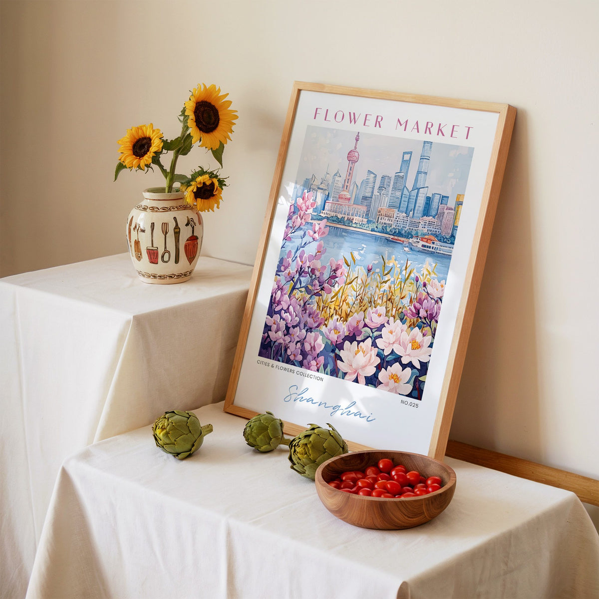 Shanghai flower market print in an oak frame leaning on a linen-draped table beside a vase of sunflowers