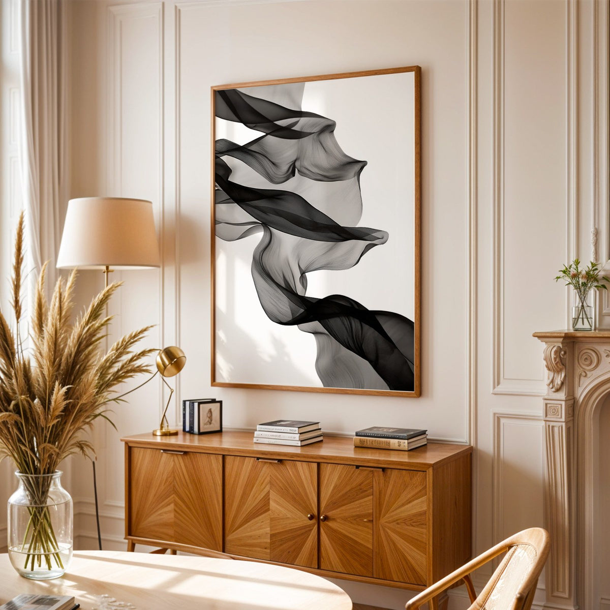 Sheer black fabric flowing across white print in an oak frame above a sunburst wood sideboard with pampas grass