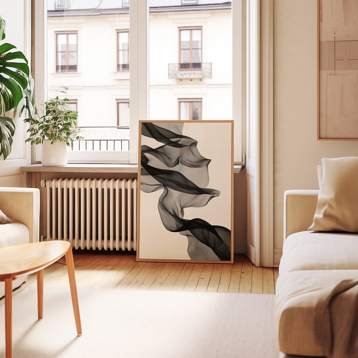 Sheer black fabric flowing across white print in an oak frame leaning by a French window in a living room