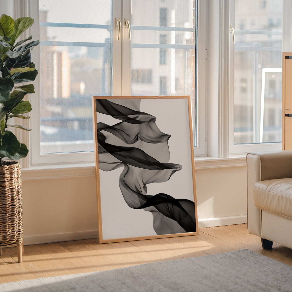 Sheer black fabric flowing across white print in an oak frame leaning on the floor beside a fiddle leaf fig