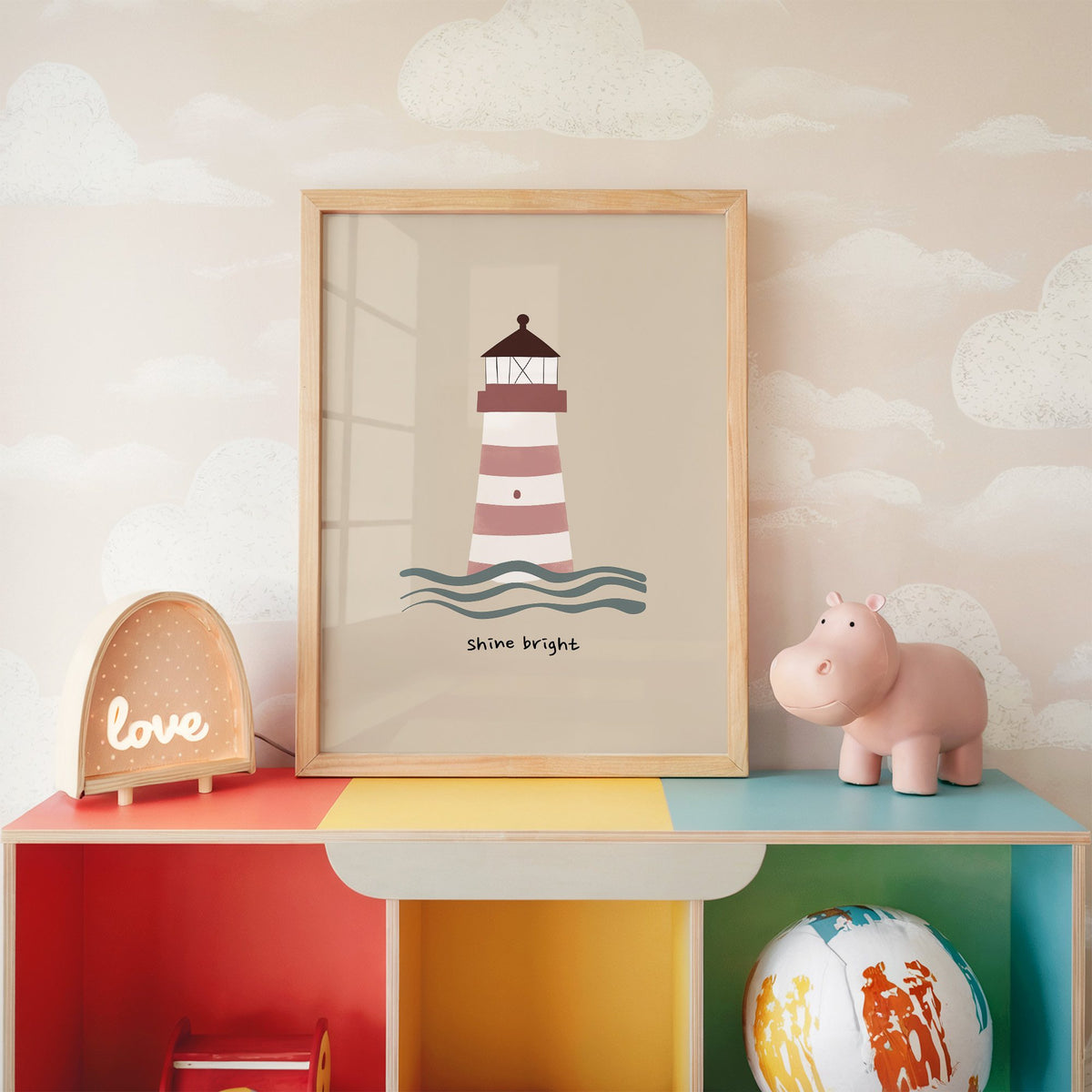 Shine bright lighthouse nursery print in an oak frame on a rainbow toy shelf against cloud wallpaper