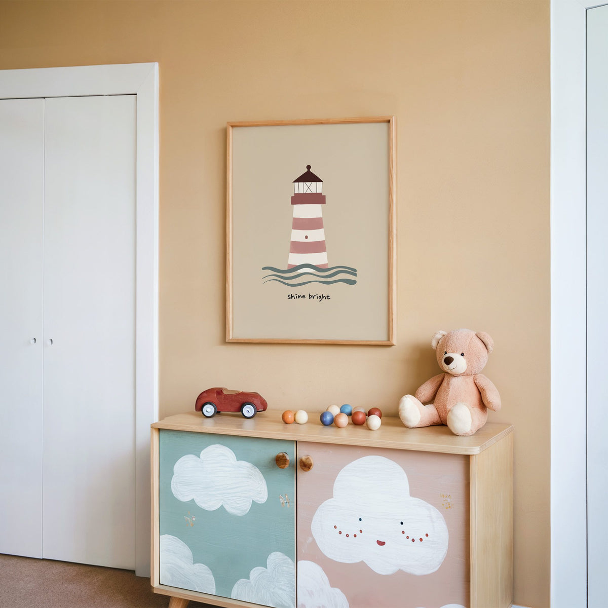 Shine bright lighthouse nursery print in an oak frame on a peach wall above a cloud-painted cabinet