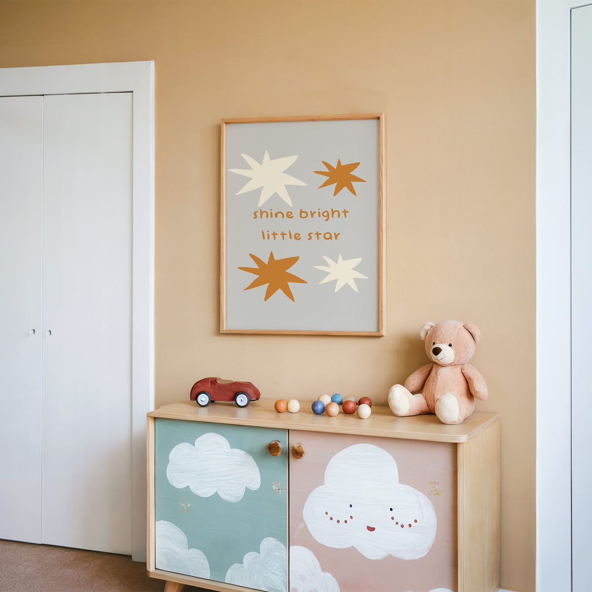 Shine bright little star nursery print in an oak frame on a peach wall above a cloud-painted cabinet