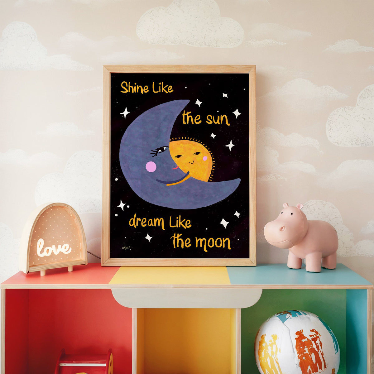 Moon hugging sun quote nursery print in an oak frame on a rainbow toy shelf against cloud wallpaper