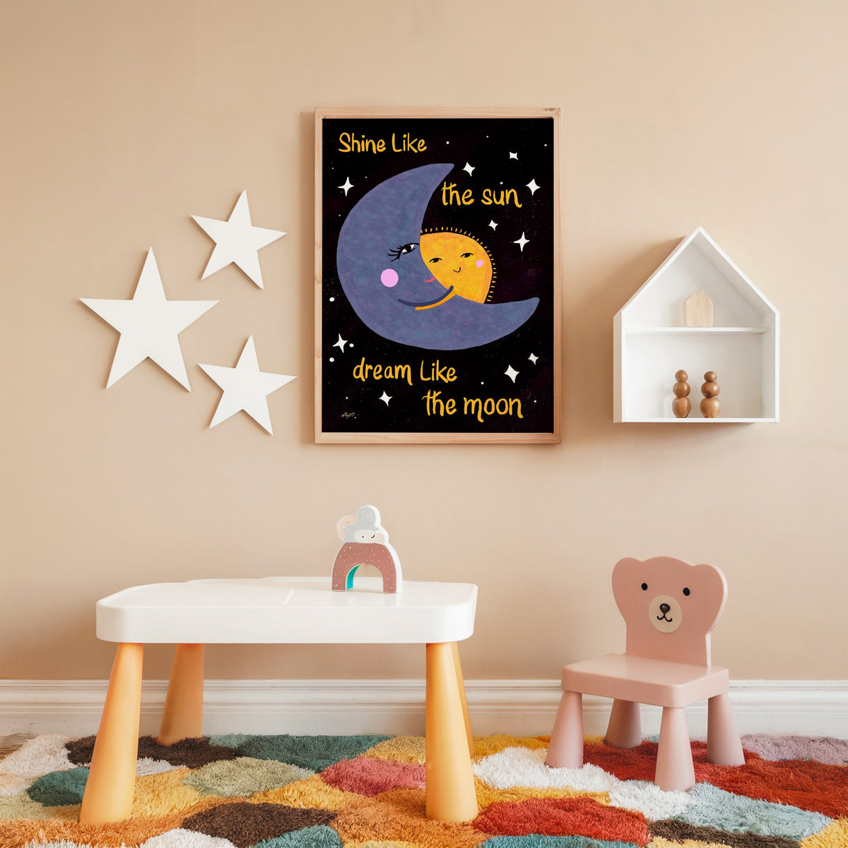 Moon hugging sun quote nursery print in an oak frame on a peach wall above a kids table with wall stars