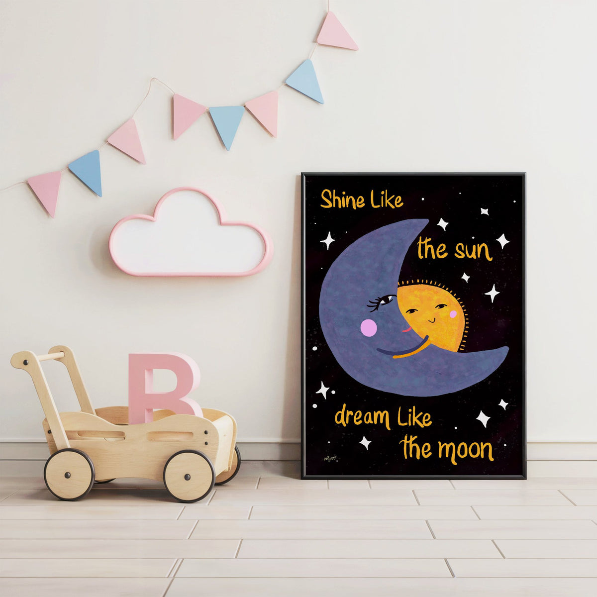 Moon hugging sun quote nursery print in a black frame under pastel bunting by a wooden baby walker