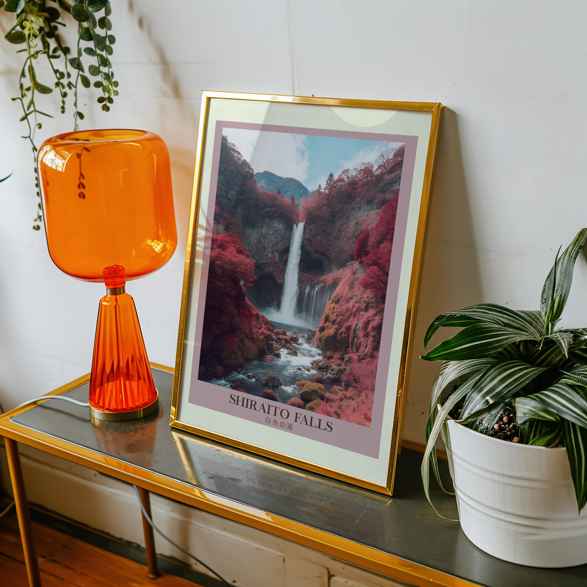 Shiraito Falls in autumn print shown in a gold frame on a console beside an orange glass lamp