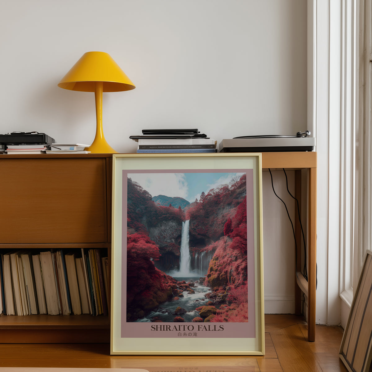 Shiraito Falls in autumn print shown in a gold frame below a teak desk with a yellow lamp