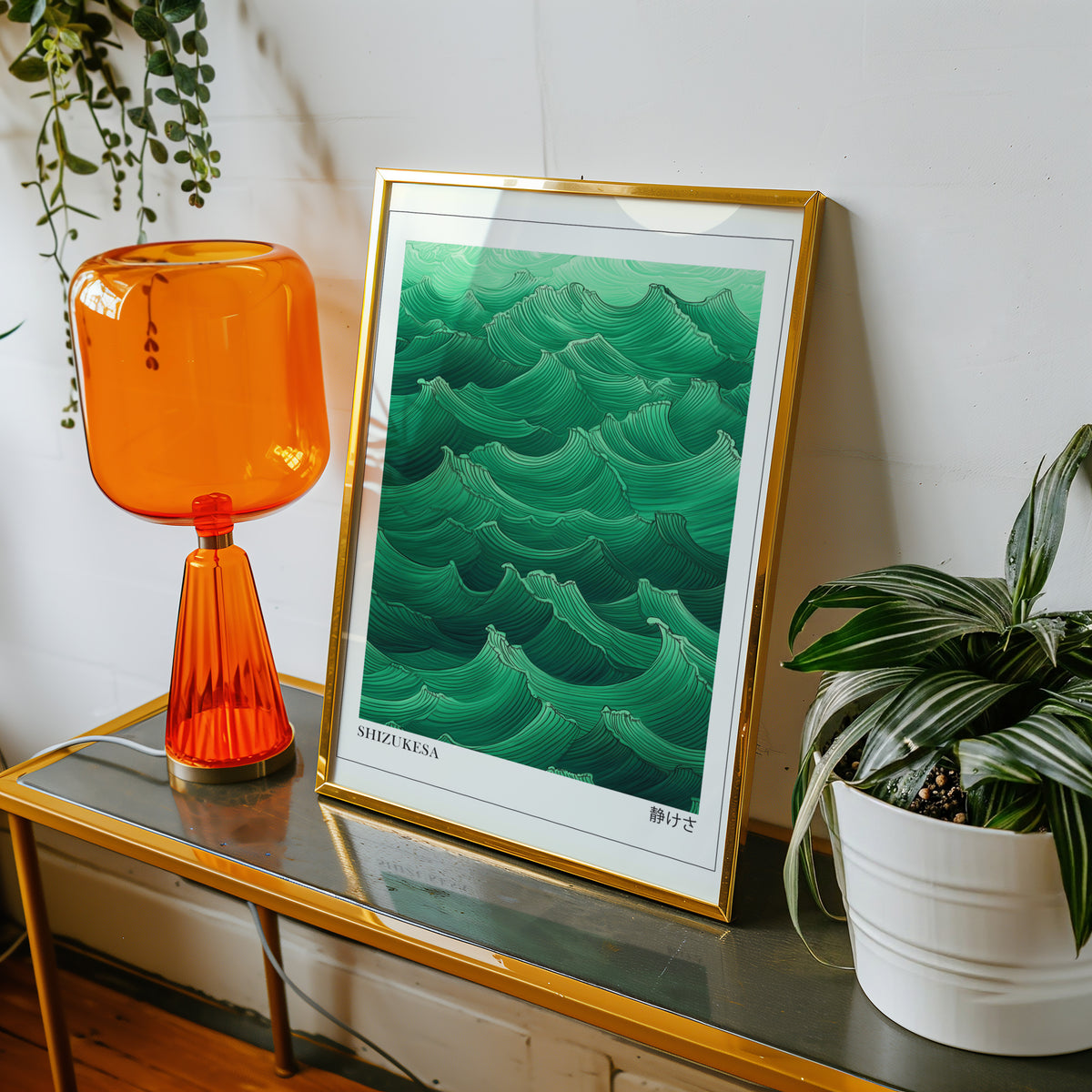 Jade green Shizukesa waves print shown in a gold frame on a console beside an orange glass lamp