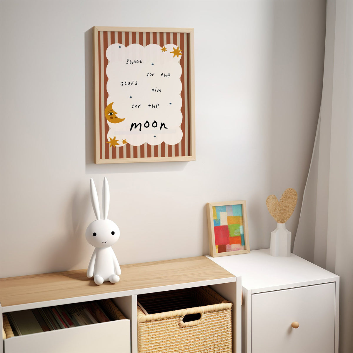 Shoot for the stars moon nursery print in an oak frame above a kids cubby shelf with a woven basket and bunny lamp