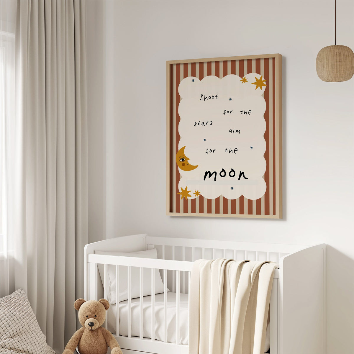 Shoot for the stars moon nursery print in an oak frame above a white crib with a teddy bear